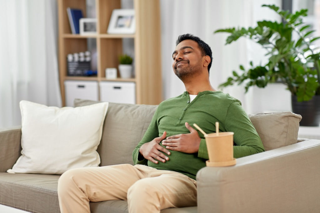 Man sitting comfortably on a couch, smiling and holding his stomach.